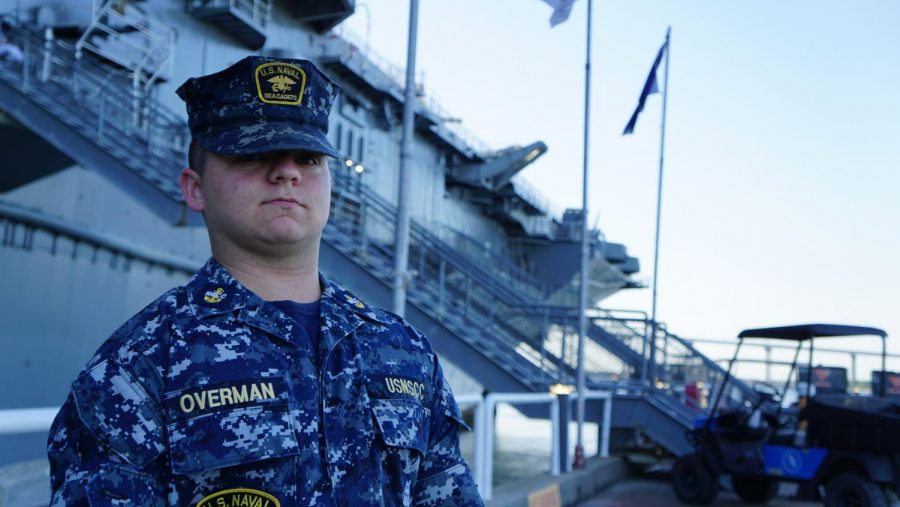 Sam Overman stands next to a naval ship in full uniform.