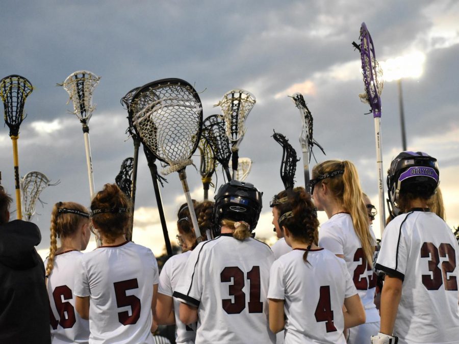 The Varsity Girls Lacrosse Team gets ready for their game against Bishop England by huddling together and raising their sticks.