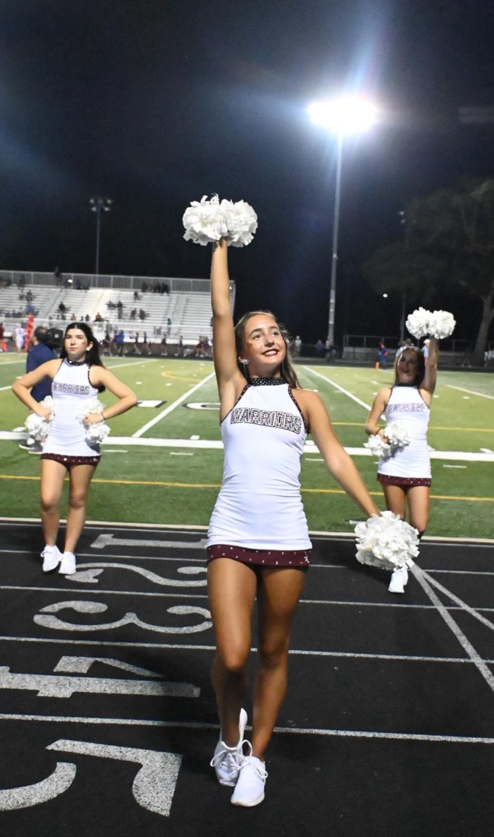 Once cheerleader lifts her pom poms up to encourage the crowd.